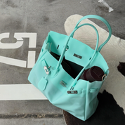 A mint green leather handbag with silver hardware, styled on a textured gray concrete surface with a white cowhide rug underneath.