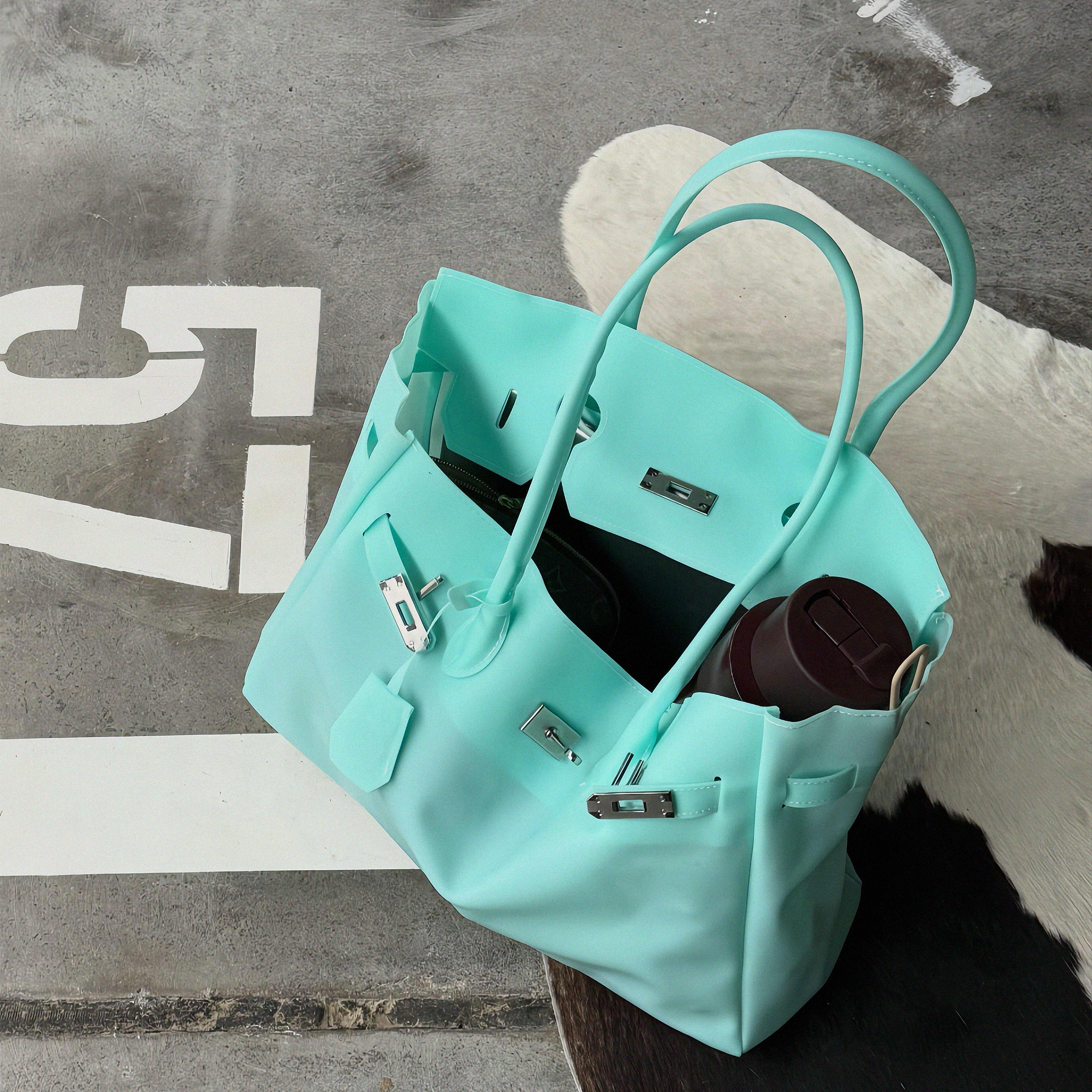 A mint green leather handbag with silver hardware, styled on a textured gray concrete surface with a white cowhide rug underneath.