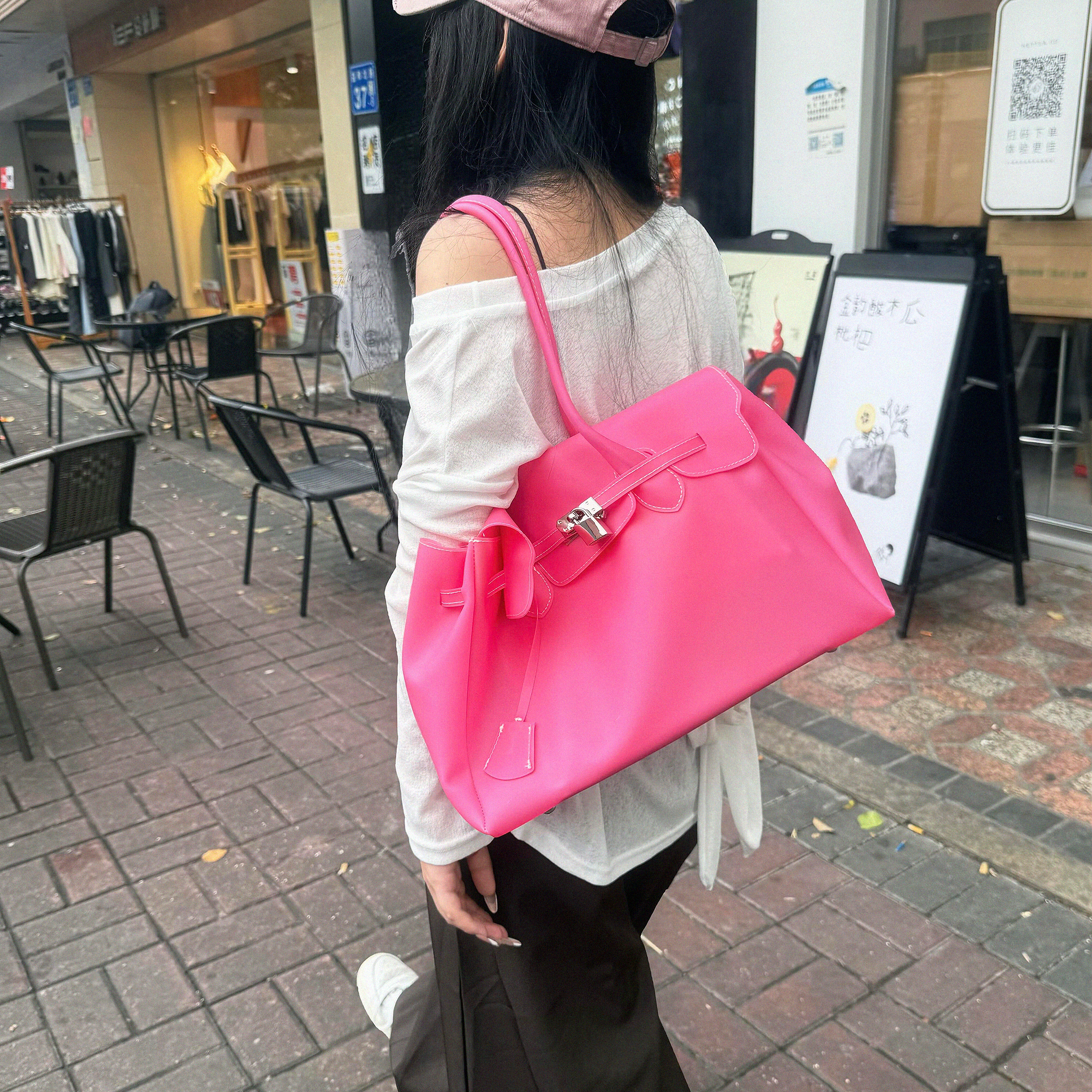 A woman carrying a large, vibrant hot pink structured handbag with a top handle and silver hardware, photographed outdoors on a city sidewalk.